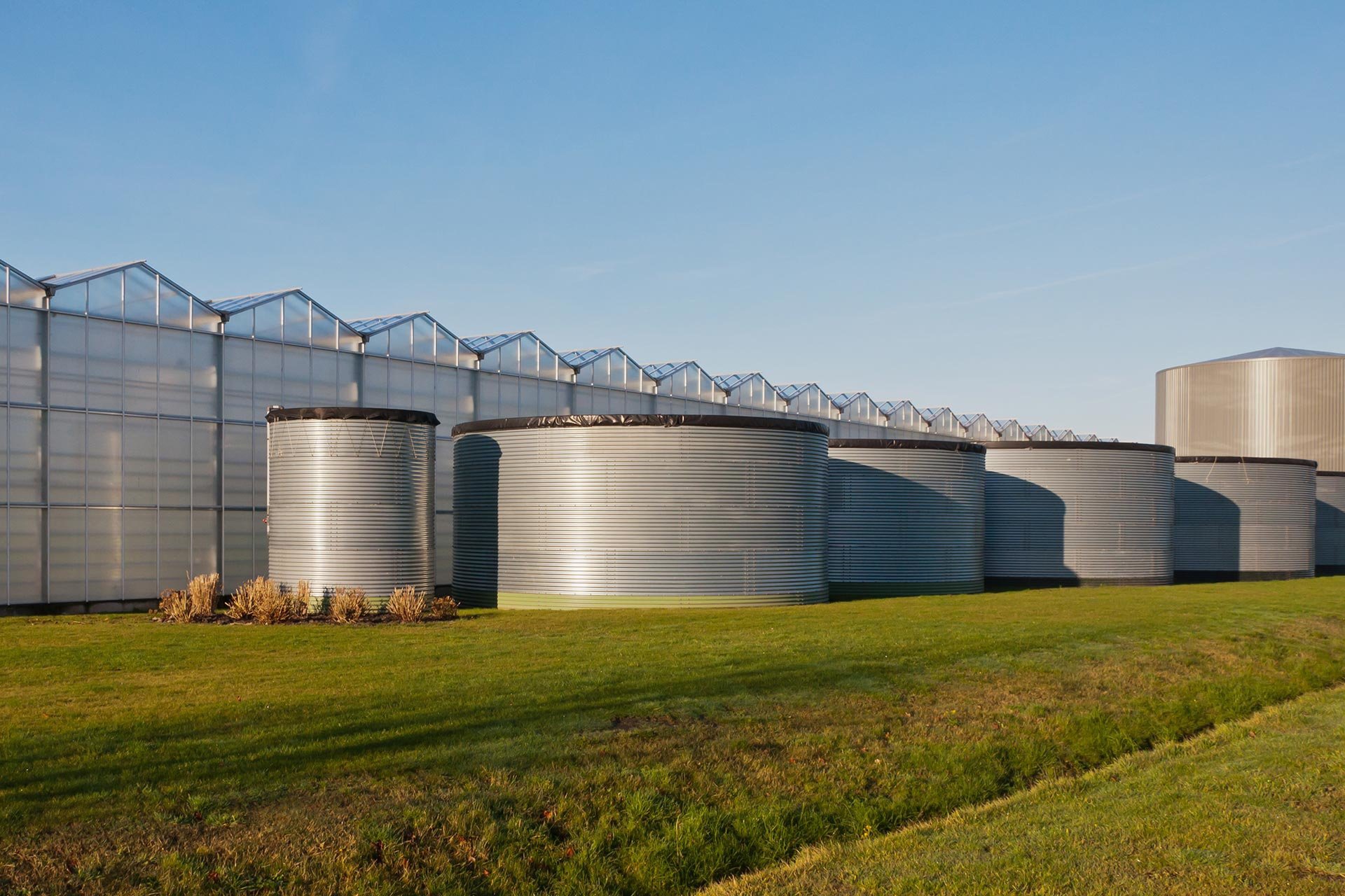 Row of metal water silos beside a professional greenhouse