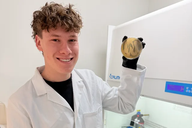 Jelle in a white lab coat holding up a petri dish next to a laminar flow cabinet in the laboratory